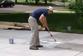 Contractor applying sealer to a concrete driveway with a long-handled roller