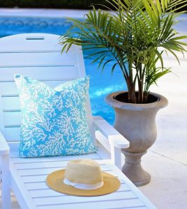 White sun lounger by a pool, with a patterned cushion, straw hat and potted palm