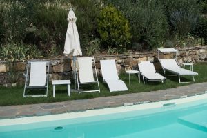 Sun loungers and a closed parasol beside a turquoise pool and stone retaining wall