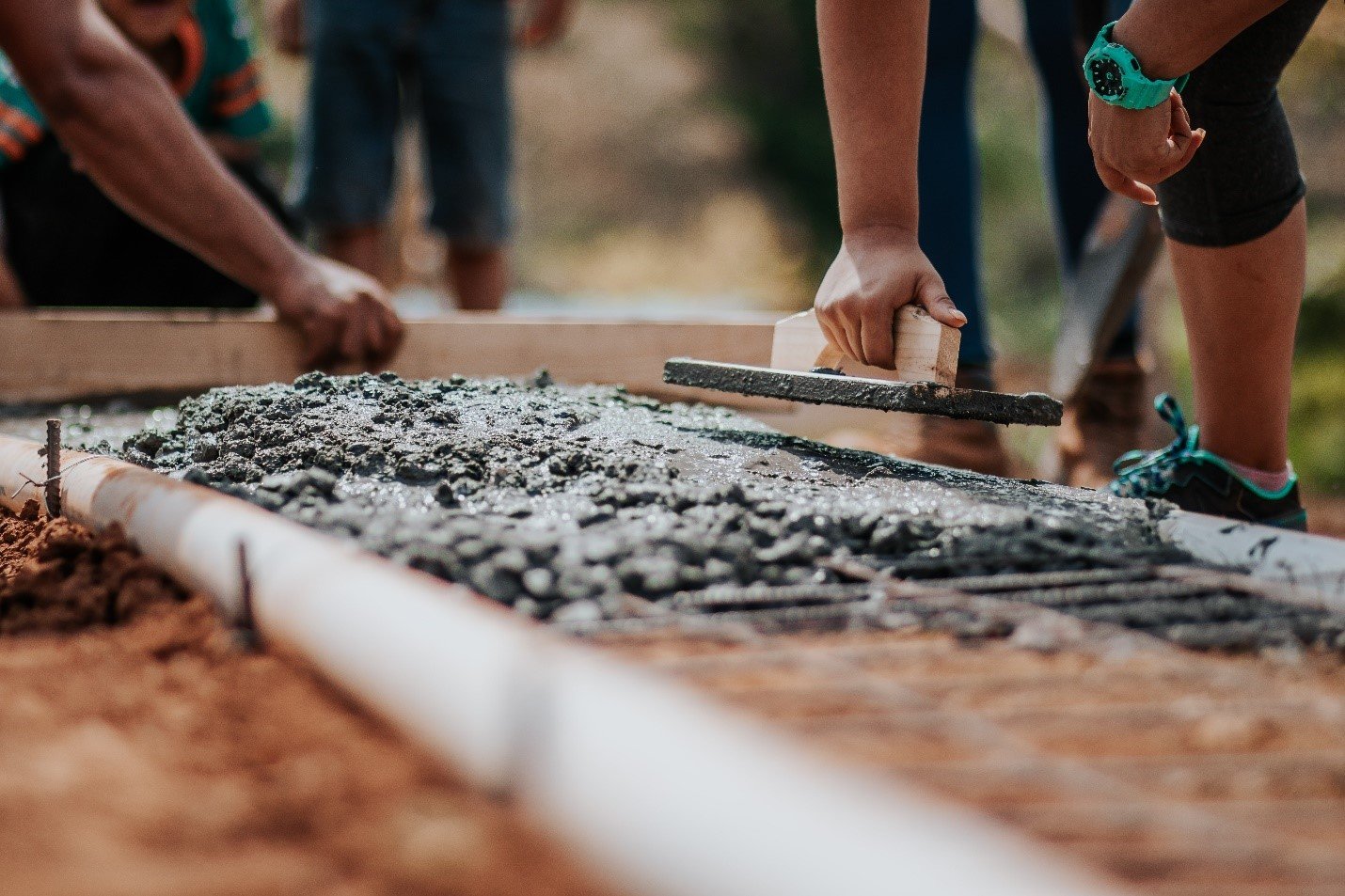 Two workers finishing wet concrete with trowels along a form board
