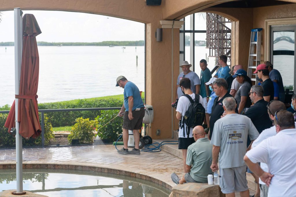 Contractors watching a live sealing demonstration on a waterfront pool deck at a Seal 'n Lock training day