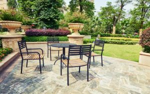 Black metal patio dining set on stone paving in a landscaped garden
