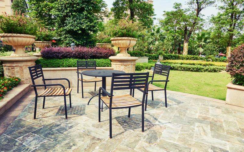 Black metal patio dining set on stone paving in a landscaped garden