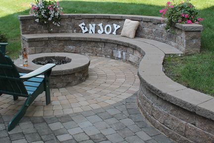 Curved paver seating wall around a fire pit, with planters and a garden chair