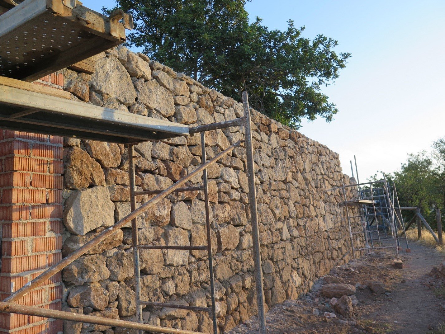 Tall rubble stone wall under construction behind scaffolding