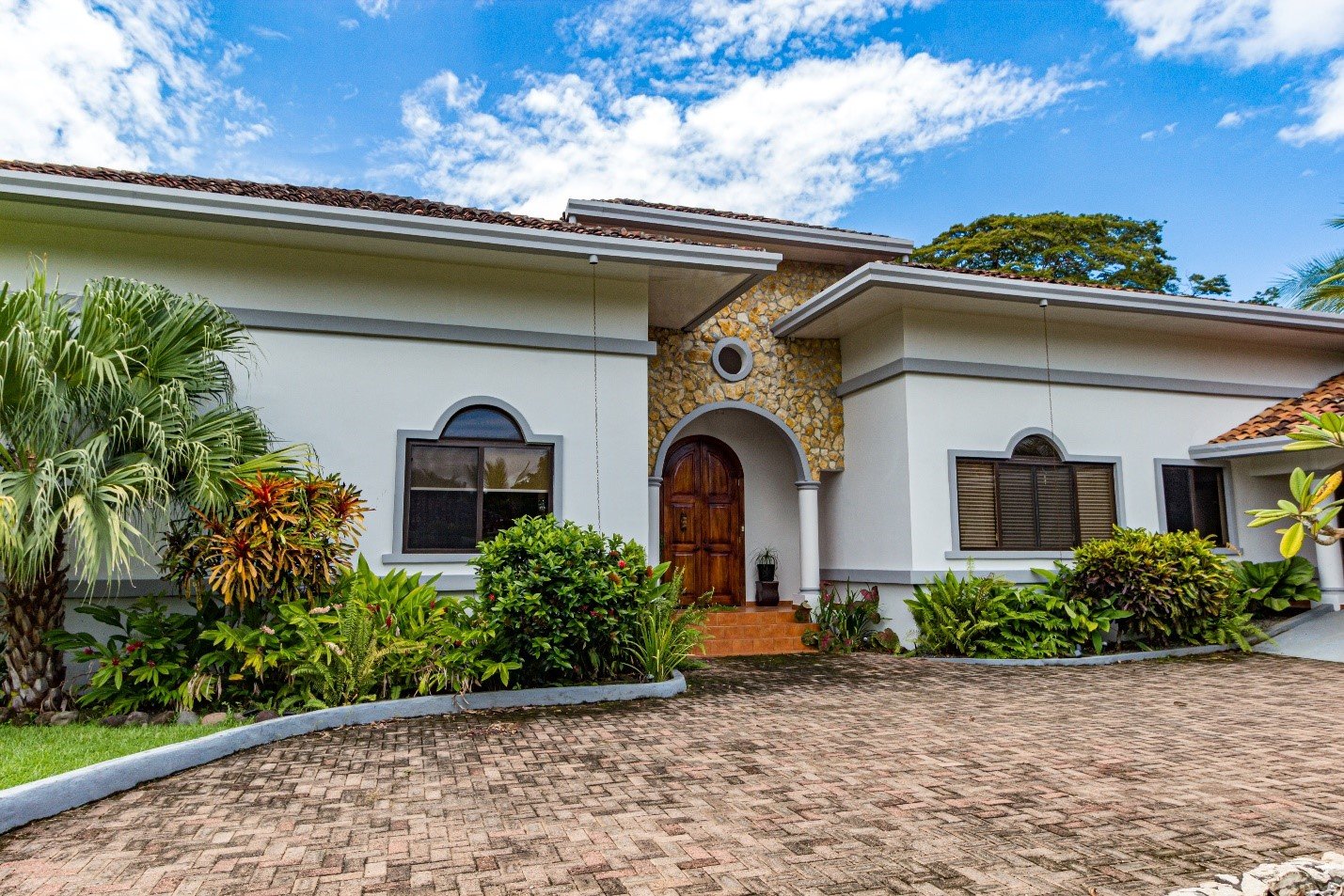 Single-storey Mediterranean-style house with a paver driveway and tropical planting