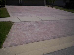 Brick paver driveway apron meeting a concrete sidewalk, the sealer faded and whitened