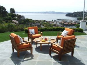 Two orange-cushioned armchairs and a coffee table on a stone patio overlooking a bay