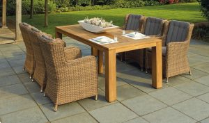 Rattan chairs around a wooden dining table on a stone patio beside a lawn