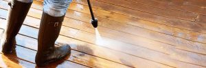 Person in rubber boots pressure-washing a timber deck