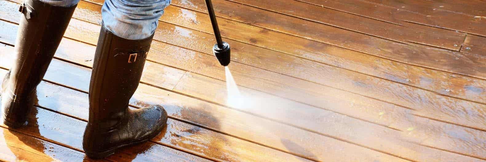 Person in rubber boots pressure-washing a timber deck