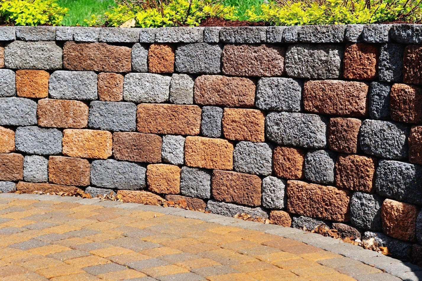 Retaining wall of multi-coloured blocks above a curved paver path