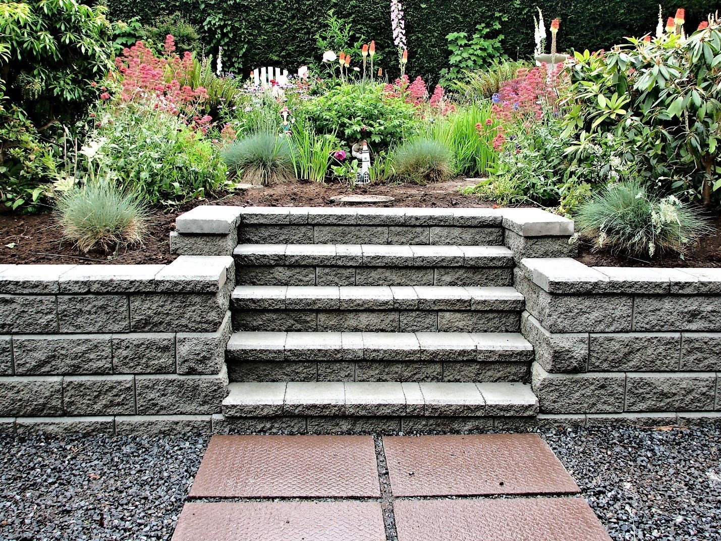 Steps set into a garden retaining wall between flowering borders