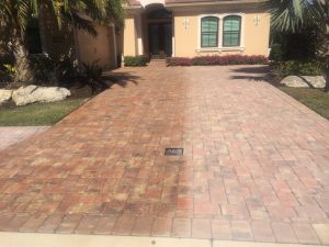 Red and tan brick paver driveway in front of a single-storey house with palms