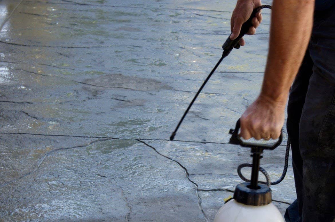Contractor spraying sealer onto concrete with a hand pump sprayer