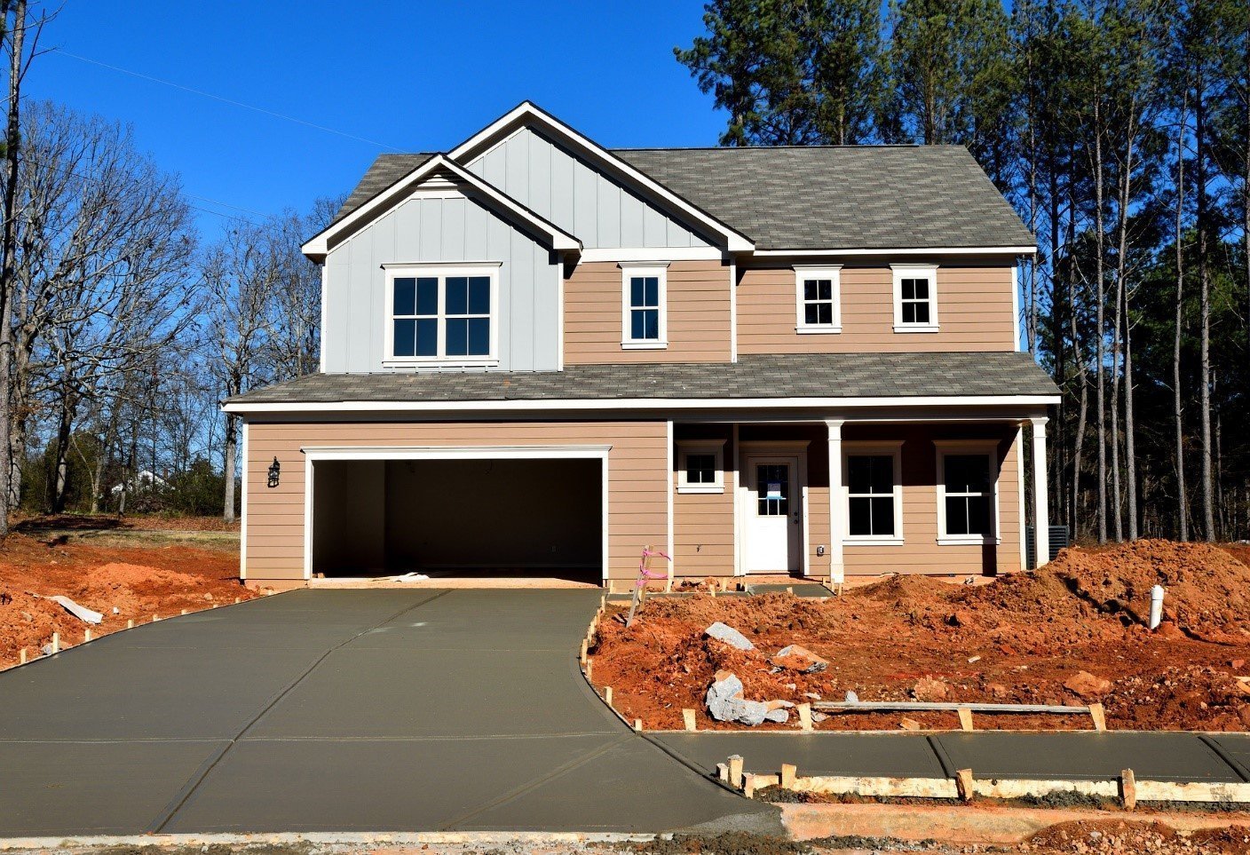 New-build house with a freshly poured concrete driveway and bare earth around it