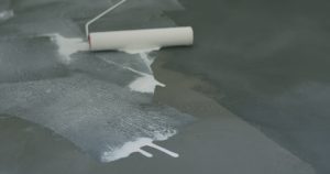 Paint roller lying in spilled white sealer on a grey floor