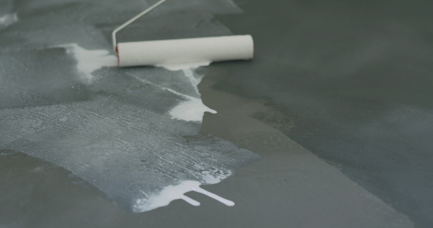 Paint roller lying in spilled white sealer on a grey floor
