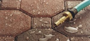 Brass hose nozzle resting on paver joints filled with sand and debris