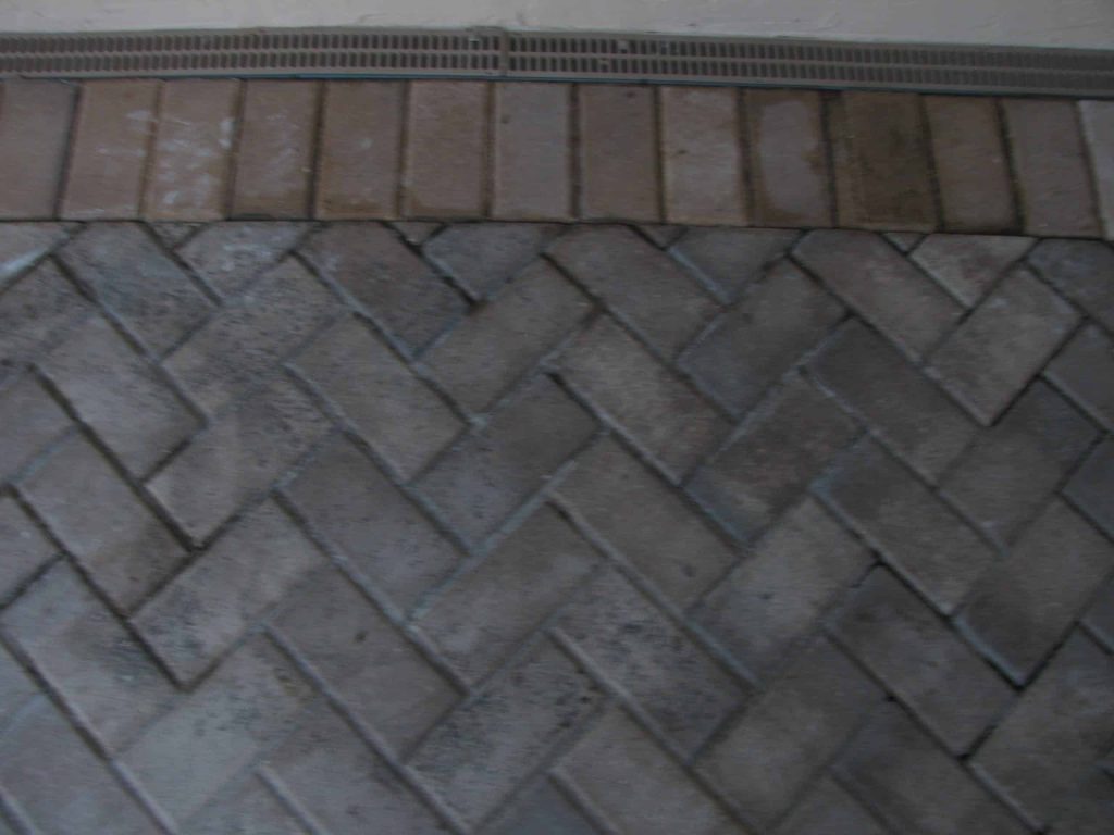 Herringbone pavers under a wall vent, grey with dirt