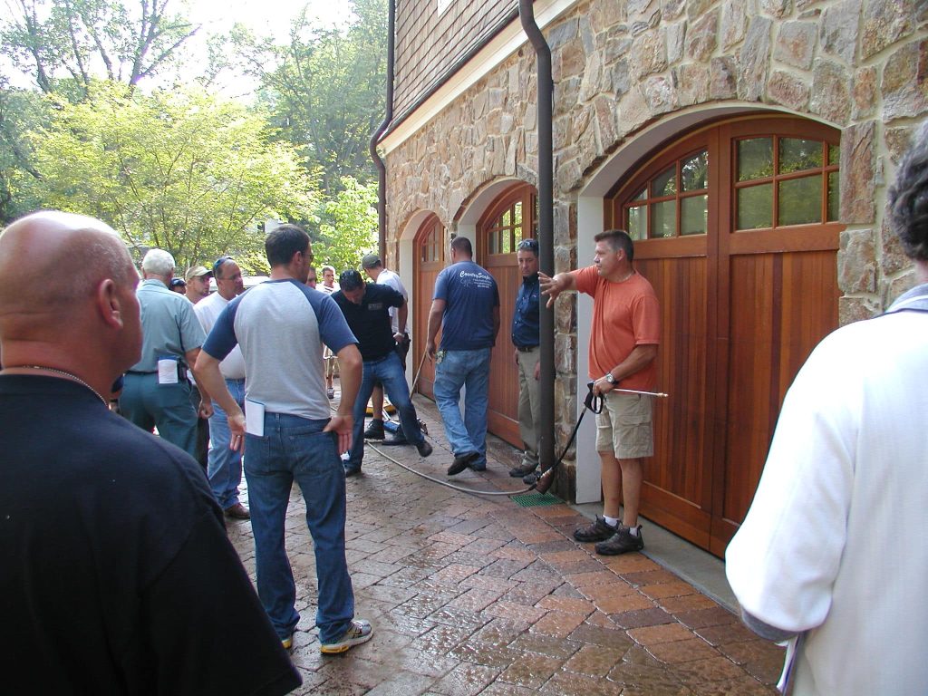 Contractors gathered by a garage while a paver driveway is worked on