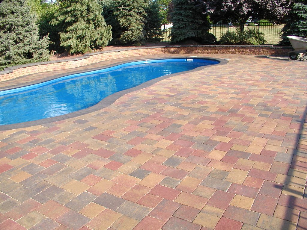 Freeform pool with a sealed paver deck in red and tan