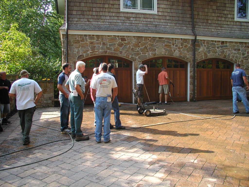 A group of contractors standing around a wet paver driveway during a Seal 'n Lock training day