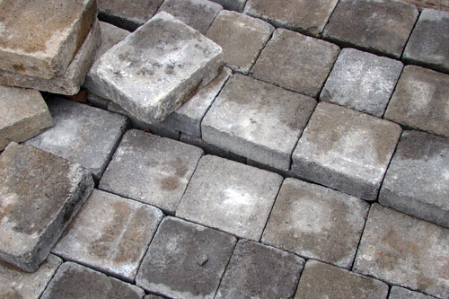 Concrete pavers with white efflorescence bloom on their faces, some stacked loose on a laid surface