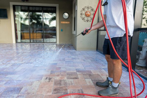 Contractor spraying a paver pool deck with a spray wand and hose
