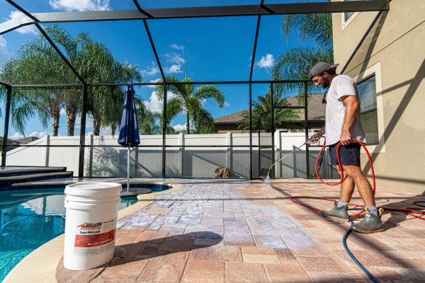 Contractor applying Seal 'n Lock PRO Max Gloss 2K sealer to a travertine paver pool deck
